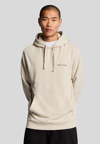 Hoodie beige avec une grande poche kangourou, capuche ajustable à cordon, et logo Lyle & Scott en lettres foncées sur la poitrine.