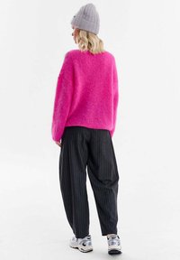 Pulover roz pufos, croială lejeră; asortat cu pantaloni negri cu dungi subțiri; căciulă gri din tricot; adidași albi cu accente negre.