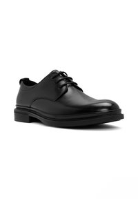 Zwarte leren dress shoe met ronde neus, een gladde textuur en vetersluiting. Beschikt over een dikke zwarte rubberen zool voor extra stabiliteit.