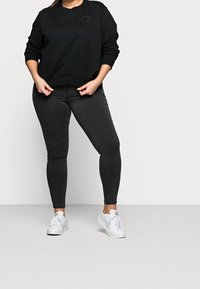 Zwarte sweatshirt met ronde halslijn en ribbelmanchetten, gecombineerd met slim-fit zwarte jeans. Witte sneakers maken de outfit compleet.