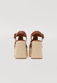 Scarpe con platform in pelle marrone con tacco in giuta intrecciata. Presentano cinturini alla caviglia con fibbia regolabile e design aperto sul retro.
