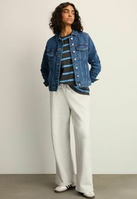 Denim jacket, blue with pockets, over a black and blue striped shirt; gray wide-leg sweatpants and gray shoes with black accents.