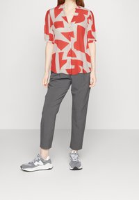 Rød og beige mønstret kortærmet bluse med krave, parret med grå skræddersyede bukser og grå sneakers med hvide detaljer.