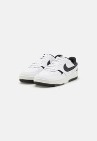 White and black athletic shoes with a smooth leather upper, perforated detailing, and contrasting black accents. Thick sole with a textured tread.