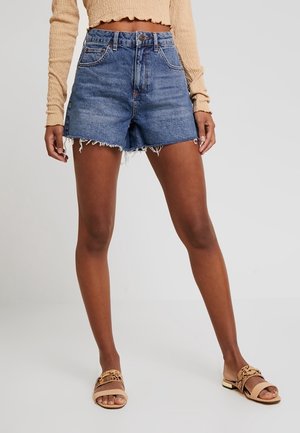 Denimshorts i medelblått med hög midja, fransad fåll och fem fickor. Matchas med beige sandaler med vävd design.