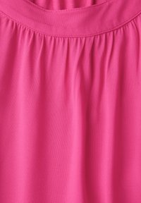 Tessuto rosa brillante con una consistenza liscia, caratterizzato da dettagli arricciati nella parte superiore. Il materiale appare leggero e leggermente lucido.
