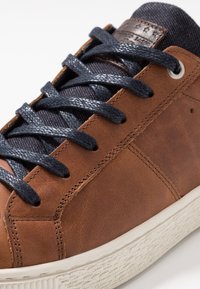 Braune Ledersneaker mit dunkelblauen strukturierten Schnürsenkeln, einer gepolsterten Zunge und einer weißen Gummisohle mit genoppter Lauffläche.