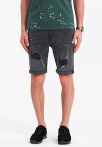 Pantalones cortos de mezclilla gris oscuro con detalles desgastados, puños doblados y dos rodillas rasgadas. Complementados con una camiseta oscura y zapatillas negras.