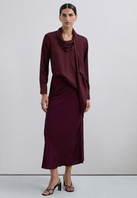 Conjunto de vestido y blusa burdeos con escote drapeado, mangas largas y una falda fluida con una abertura lateral y detalles bordados.