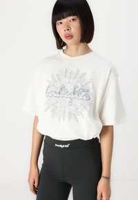 Maglietta bianca over size con un design grafico argentato lucido sulla parte anteriore, abbinata a leggings neri a vita alta con un elastico con logo.