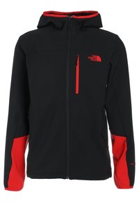 Veste noire à capuche avec accents rouges, fermeture éclair sur la poche poitrine, et logo The North Face sur la poitrine gauche.