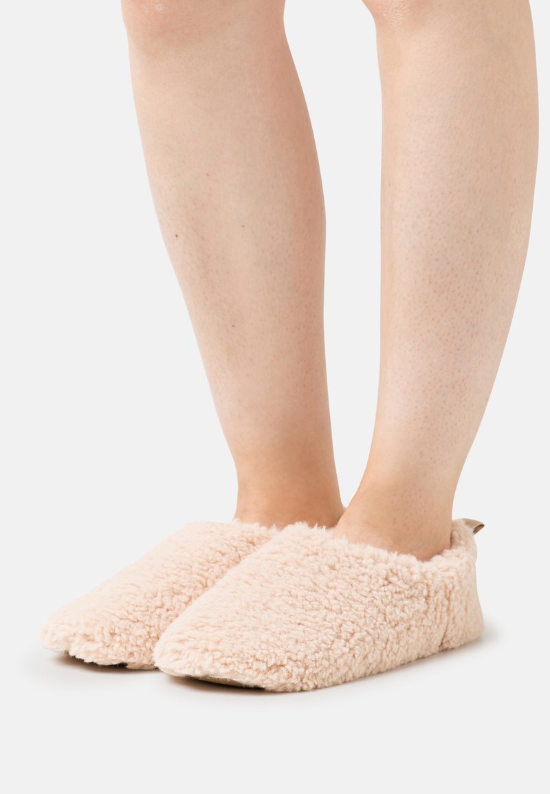 Light pink fluffy slippers with a soft, textured exterior and rounded toe design, featuring an open back and minimalistic brown tab detail.