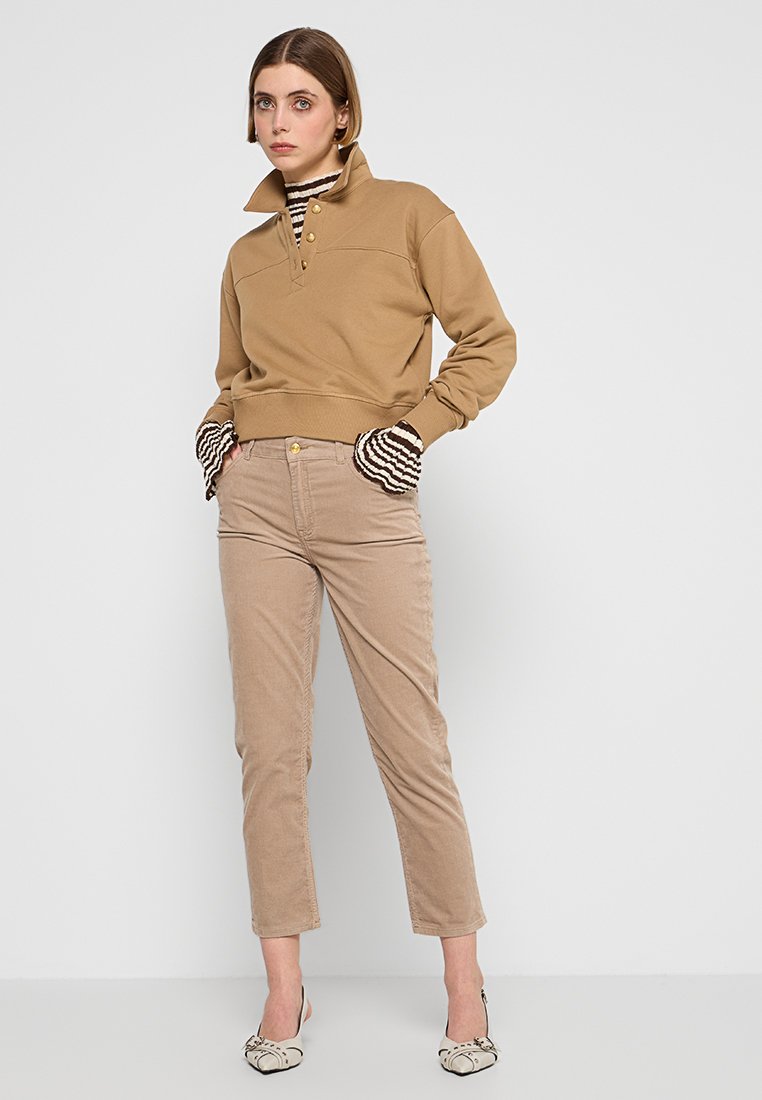 Beiger Pullover mit hohem Kragen und drei Knöpfen, kombiniert mit beigen Cordhosen. Gestreifte Bündchen sorgen für kontrastierende Details an den Ärmeln.