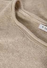 Suéter beige de punto con un patrón texturizado, cuello ancho y ajuste ligeramente holgado. Cuenta con una etiqueta de cuidado cosida en el cuello.