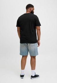 Sort crewneck t-shirt kombineret med lyseblå denim shorts. Modellen har sorte sneakers med hvide såler og ankellange hvide sokker på.