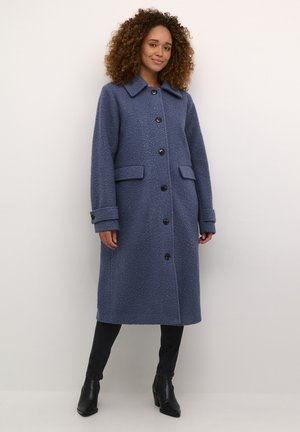 Manteau en mélange de laine bleu clair avec un col, des boutons sur le devant, deux poches latérales et un tissu texturé, arrivant jusqu'au milieu du mollet.
