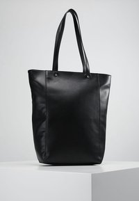 Czarna skórzana torba typu tote z dwoma długimi uchwytami, gładką fakturą, minimalistycznym designem oraz widocznymi przeszyciami po bokach.