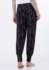 Svarta byxor med elastisk midja, prydda med ett vitt abstrakt träådringsmönster, med smalnande anklar och mjukt, lätt tyg.