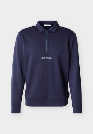 Pull-over à manches longues bleu marine avec une fermeture éclair au quart, col, bandes blanches sur les épaules, et logo "Calvin Klein" centré sur la poitrine.
