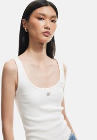 Witte geribde tanktop met een ronde halslijn en een kleine vlinderapplicatie in het midden. Glad textuur en aansluitende pasvorm.