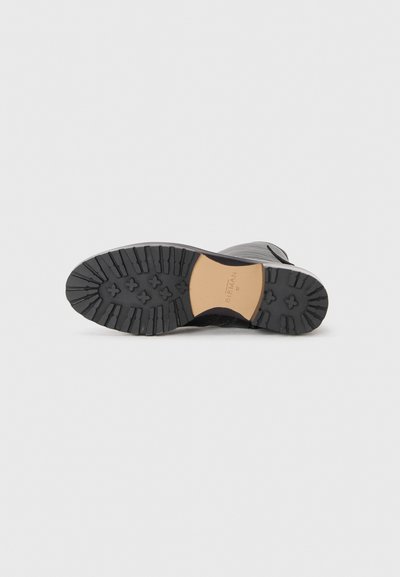Black rubber sole with deep treads, featuring a contrasting beige section. The upper part is textured, with a sleek, rounded design.
