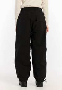 Zwarte, hoge cargo-broek met een elastische tailleband. Beschikt over een achterzak en taps toelopende benen. Het materiaal lijkt duurzaam met een gladde textuur.