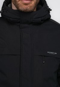 Schwarze wasserdichte Jacke mit hohem Kragen, verstellbarem Kordelzugkapuze und markenspezifischen Details. Verfügt über Reißverschlüsse und eine glatte Textur.
