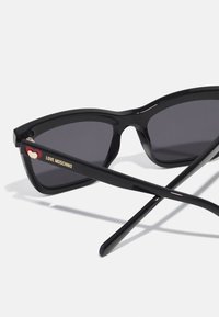 Black cat-eye sunglasses with dark lenses and glossy plastic frame. Features gold text "LOVE MOSCHINO" and a heart accent on the arm.