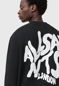 Schwarzer, übergroßer Sweatshirt aus Baumwolle mit großem weißen Textdesign auf der Rückseite, das "ALLSAINTS LONDON" liest. Der Text hat eine fließende Form.