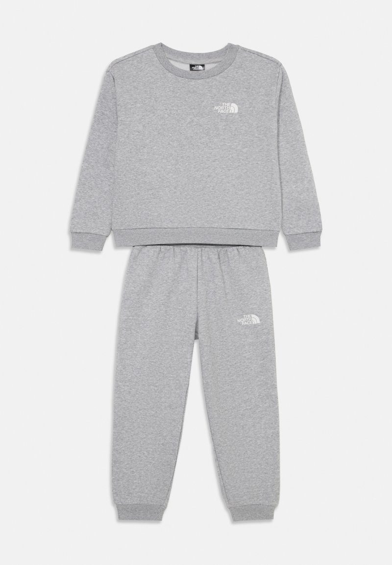 Pelēks treniņtērps, kas izgatavots no mīksta auduma, ar apaļu kaklu, ribotām aprocēm un mazu baltu logotipu abās detaļās.