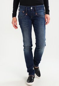 Jeans in denim blu scuro con vestibilità slim, caratterizzati da cinque tasche, leggera scoloritura sulle ginocchia e accenti in tonalità rame.