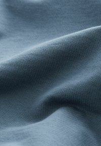 Tissu doux bleu clair avec une texture fine tricotée montrant des plis légers et des détails de surface lisses.