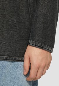 Zwarte denim lange mouwen top met een gestructureerde afwerking. Heeft een omzoomde manchette en toont een deel van lichtblauwe denim eronder.