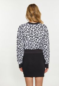 Top de manga larga con estampado de leopardo en blanco y negro, combinado con una falda negra ajustada. Presenta puños y cinturilla acanalados para un ajuste ceñido.