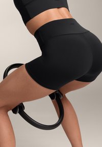 Shorts de sport negri cu talie înaltă, textură fină, asociate cu un inel de exerciții negru. Design simplu și funcțional.