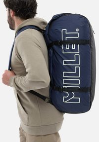 Sac à dos marin avec le logo "Millet" blanc, doté de bretelles réglables, d'une construction en tissu durable et d'une forme cylindrique.