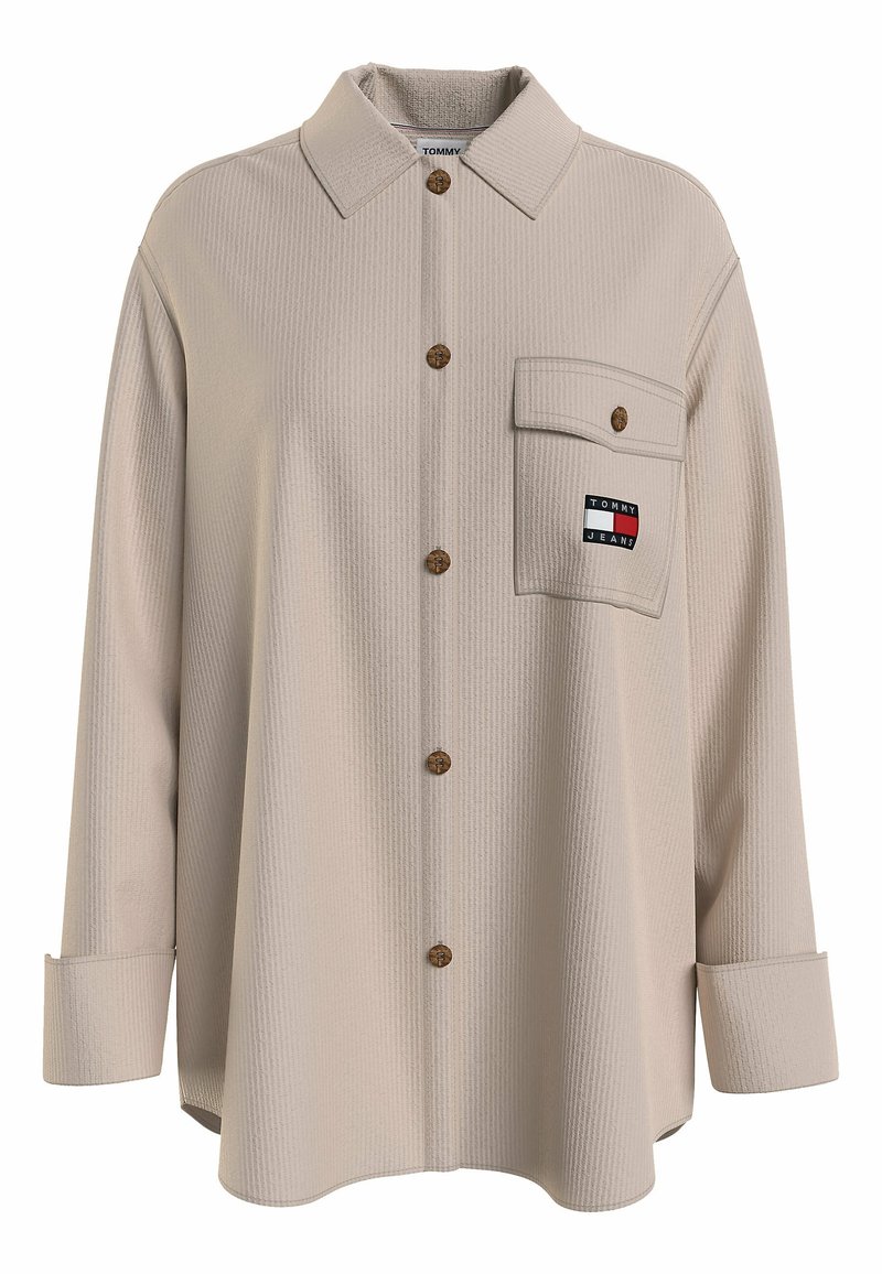 Camicia beige con bottoni, caratterizzata da un design testurizzato, bottoni in legno e una tasca sul petto con una patch del logo. Maniche lunghe con polsini.