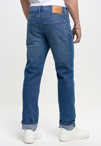 Jeans in denim blu con taglio dritto, dotati di un'etichetta in pelle marrone sulla vita e sulle tasche posteriori. I risvolti mostrano un orlo più chiaro.