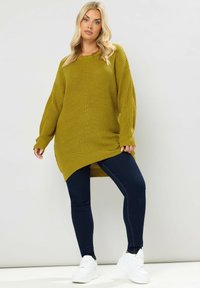 Ylätunnus ribbiknitti neule, oliivinvihreä, pitkät hihat ja epäsymmetrinen helma, yhdistetty tummansinisiin tiukkoihin farkkuihin ja valkoisiin tennareihin.