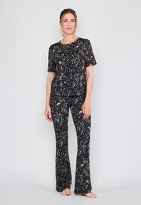 Zwarte en gouden gelooide loungeoutfit met een T-shirt met korte mouwen en flared broeken, gemaakt van zachte, gestructureerde stof.