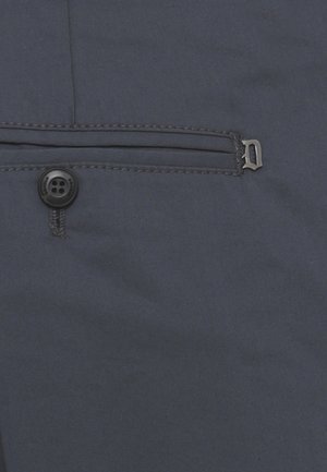 Primo piano di tessuto scuro con un piccolo bottone nero e una tasca orizzontale cucita con una cerniera di metallo.