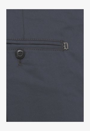 Primo piano di tessuto scuro con un piccolo bottone nero e una tasca orizzontale cucita con una cerniera di metallo.