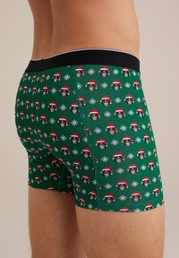 Zaļi bokseršorti ar zīmējumu, kurā redzami pērtiķi Ziemassvētku cepurēs un baltas sniegpārsliņas. Mīksta auduma, ar melnu elastīgu jostu.