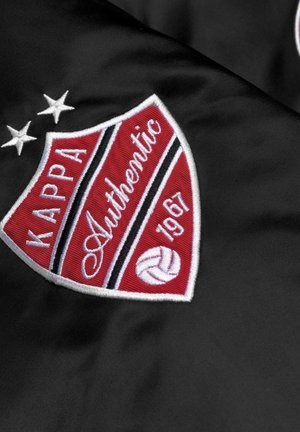 Tessuto nero con logo a scudo ricamato in rosso e bianco con la scritta "KAPPA Authentic" e l'anno "1967" accanto a un'icona di pallavolo.