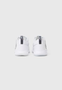 Para białych sneakersów Nike widziana z tyłu, z szarymi logo swoosh i pętelkami na jednolitym jasnym tle.