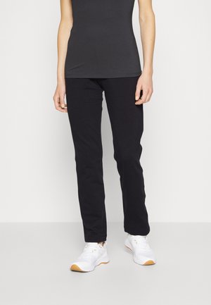 Zwarte stretchbroek met een slim fit, voorzien van een vlakke tailleband. Gepaard met een nauwsluitende donkere top en witte sneakers. Glad textuur van de stof.