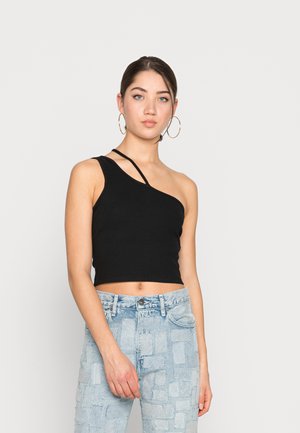 Top cropped preto com uma alça, combinado com jeans azul claro com um padrão de retalhos. Textura suave, ajuste casual.