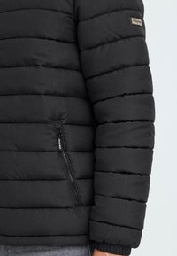 Melnā pūkainā jaka ar šuvju tekstūru, ar rāvējslēdzēja kabatu un elastīgiem roku galiem. Minimālistisks dizains, izturīgs materiāls, eleganta silueta.