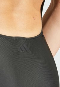 Camiseta de tirantes deportiva negra con una textura suave, diseño ajustado y un discreto logo negro de adidas en la parte posterior.