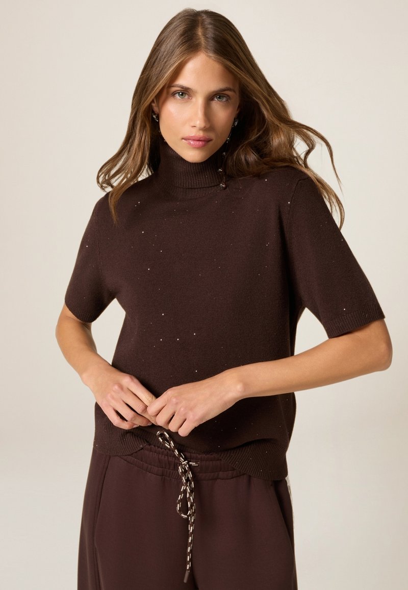 Suéter de cuello alto marrón de manga corta con detalles salpicados, combinado con pantalones marrones con cordón. Textura suave, ajuste relajado.